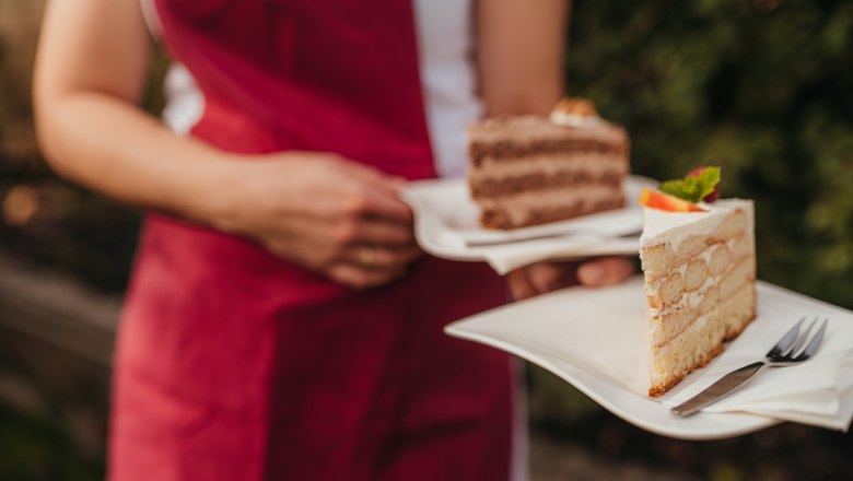Hausgemachte Torten, © Niederösterreich Werbung/Daniela Führer Person in roter Schürze hält zwei Teller mit Tortenstücken.