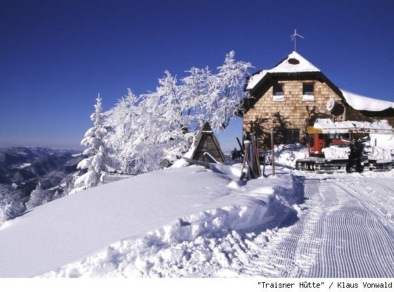 Traisnerhütte, © zVg Snow-covered mountain hut with snow-covered trees and a clear blue sky.