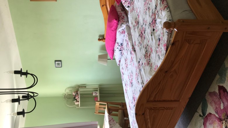 TDR-HausMaier bedroom, © Alicia Maier Bedroom with double bed, green walls, floral bedding, table with chairs, curtains and chandelier.