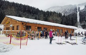 Fuchswaldhütte, © Haus Österreich Skihütte im Schnee mit Skifahrern und Ausrüstung davor.