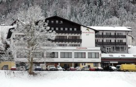 Sporthotel am Ötscher, © Iby & Bogi Matayas Touristik GmbH Ein verschneites Hotelgebäude mit der Aufschrift 'Sporthotel' und 'Cafeteria', umgeben von schneebedeckten Bäumen und geparkten Autos.