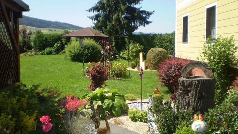 Haus Gerti, © Familie Hödelsberger Ein gepflegter Garten mit Blumen, Sträuchern und einem gelben Haus im Hintergrund.