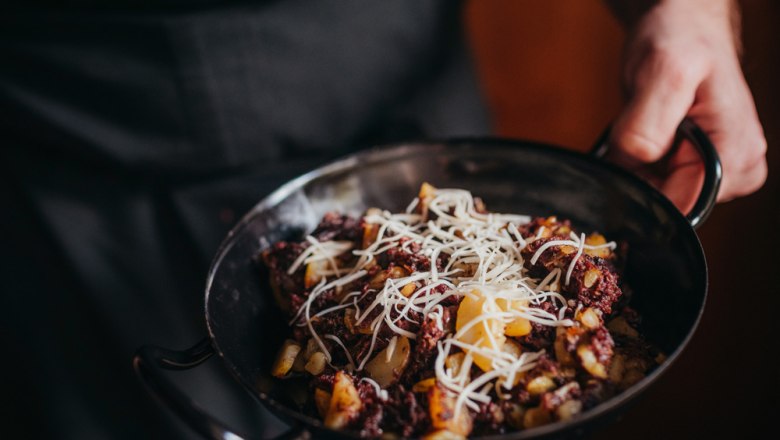 Blunzengröstl with sauerkraut, © Niederösterreich Werbung/Daniela Führer One person holds a pan of Blunzengröstl, garnished with grated cheese.
