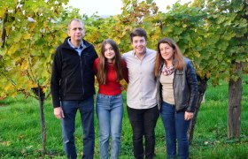 Familie Poyntner, © Familie Poyntner Vier Personen stehen lächelnd vor Weinreben im Freien.