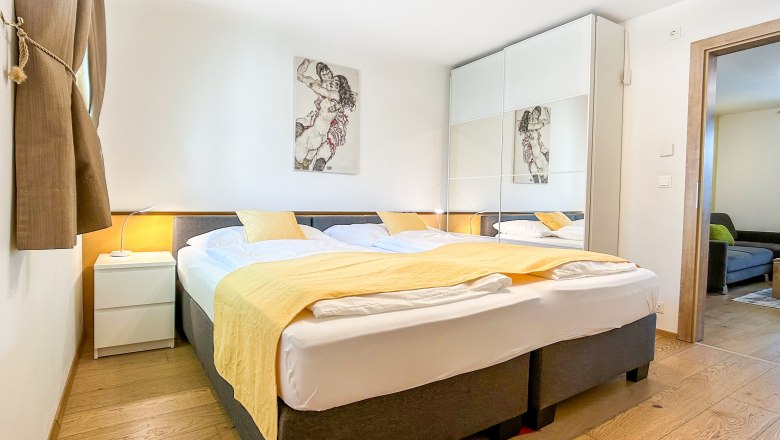 Haus Morgensonne Schlafzimmer, © Fam. Pauker Modernes Schlafzimmer mit Doppelbett, gelber Bettdecke und großem Kleiderschrank mit Spiegeln.