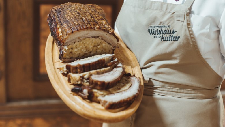 Stuffed breast of Duroc pork, © Niederösterreich Werbung/David Schreiber Stuffed pork breast on a wooden platter, served by a person in an apron.