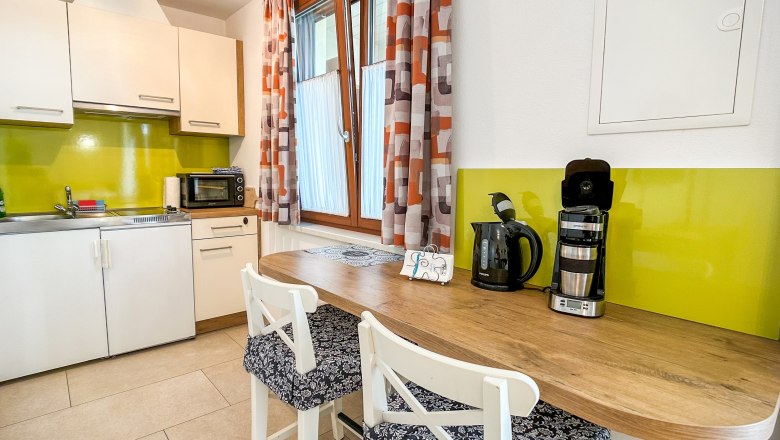 Haus Morgensonne Küche, © Fam. Pauker Moderne Küche mit grüner Rückwand, weißen Schränken, Holztheke und Kaffeemaschine.