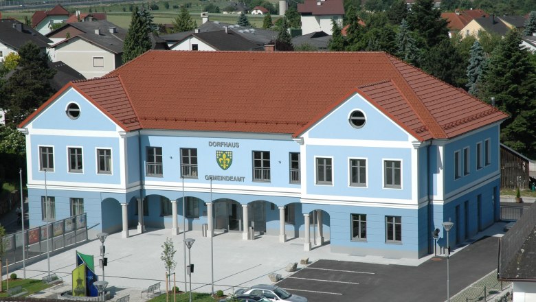 Viehdorf, © Gemeinde Viehdorf Blaues Gebäude mit rotem Dach, beschriftet als Dorfhaus Gemeindeamt, umgeben von Häusern und Bäumen.