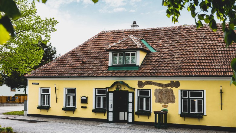 Figl restaurant in St. Pölten (Ratzersdorf), © Niederösterreich Werbung/David Schreiber Yellow building with red roof tiles and green shutters, surrounded by trees.