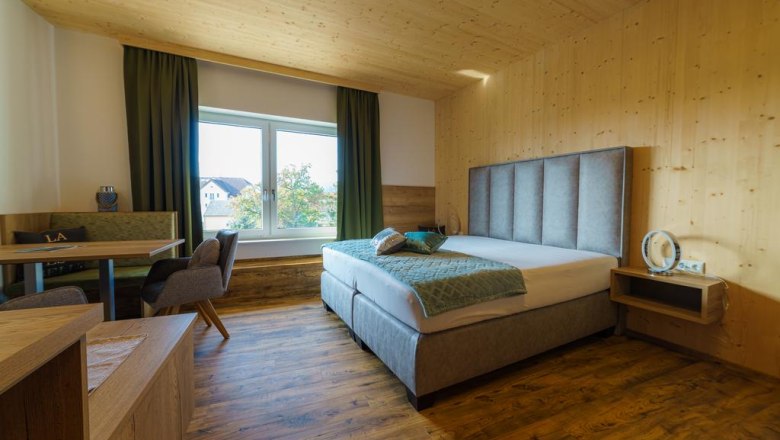 Zimmeransicht, © Familie Harrauer Modernes Hotelzimmer mit Doppelbett, Holzwänden und großem Fenster.