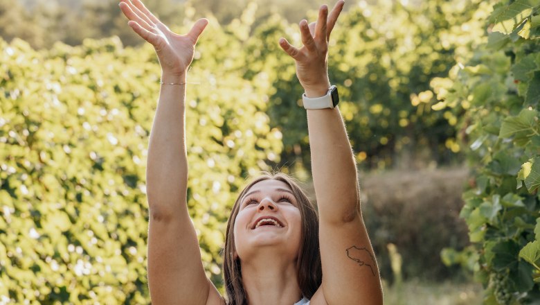 TDR-Winery Haimel, © Cornelia Wurst Woman throws wine bottle into the air in a vineyard.