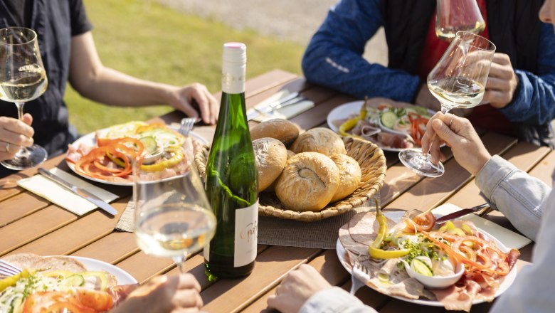 Wine taverns, © Doris Schwarz-König People enjoy wine and snacks outdoors at a wooden table.