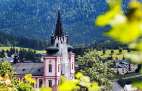 Blick auf die Basilika Mariazell, © weinfranz.at Basilika Mariazell vor bewaldeten Hügeln, umgeben von grüner Landschaft.