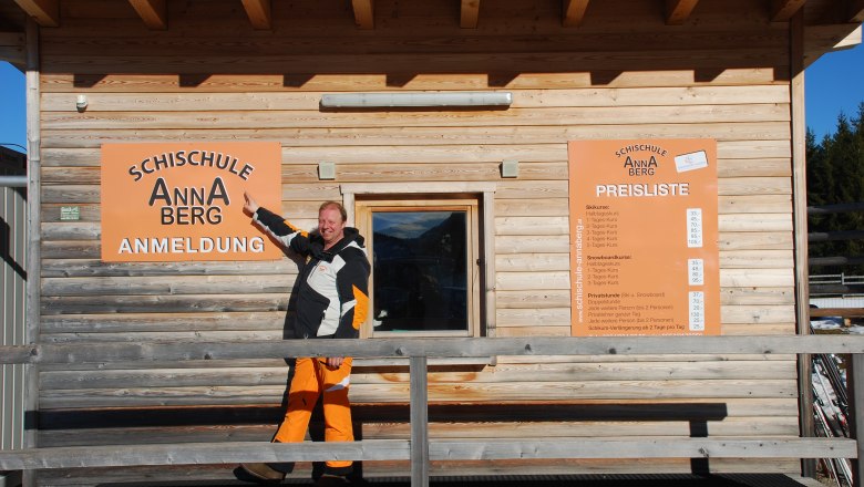 Ski school Annaberg, © © NÖ-BBG A man points to a sign for the Annaberg ski school in front of a wooden building.