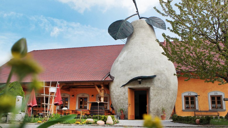 To the stone pear, © weinfranz.at Building with pear-shaped entrance and red roof, surrounded by plants.