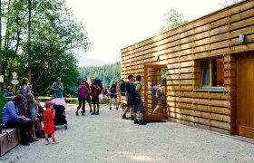 Stapelhaus Eingang, © Harddecor Architektur Menschen vor einem modernen Holzgebäude in einer Waldumgebung.