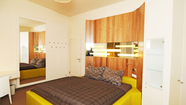 Haimel Winery, © Fotostudio Andreas Kraus Modern furnished bedroom with yellow bed and wood paneling on the wall.