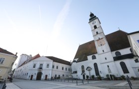 Pfarrkirche, © schwarz-koenig.at Pfarrkirche mit Uhrturm und angrenzenden Gebäuden auf einem leeren Platz.