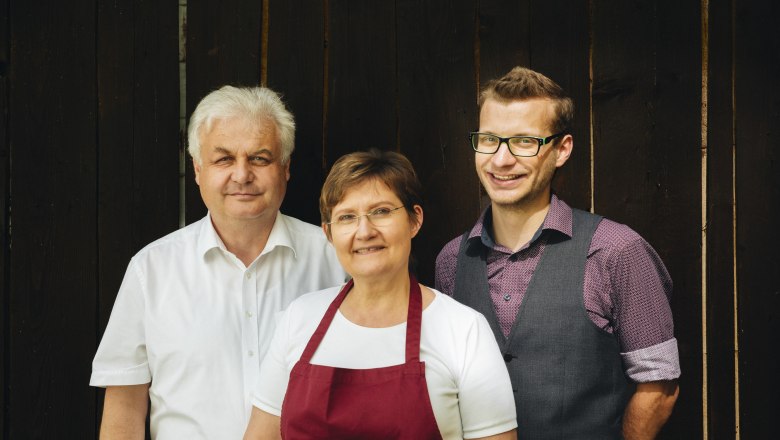Ettel family, © Niederösterreich Werbung/Julius Hirtzberger Three people stand in front of a wooden background, two men and a woman in the middle.
