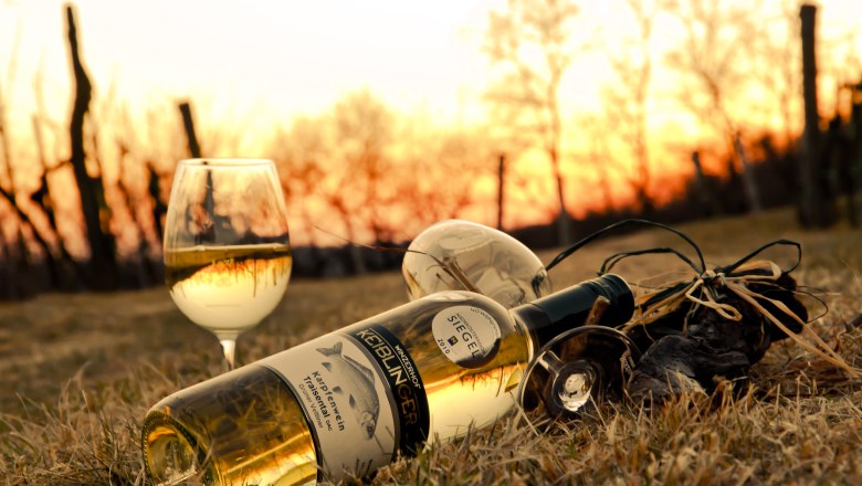 Wein vom Winzerhof Keiblinger, © Winzerhof Keiblinger Weinflasche und Glas im Gras bei Sonnenuntergang.