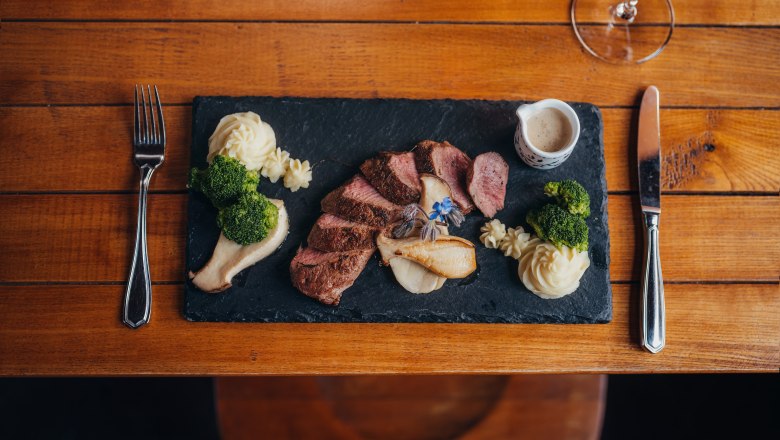 Pink saddle of venison, Grestner oyster mushrooms, truffle puree, juniper berry sauce, © Niederösterreich Werbung/Daniela Führer Gourmet dish on a slate with meat, puree, broccoli and sauce.