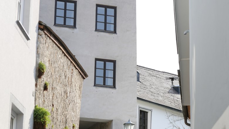 Burgerhof gate, © schwarz-koenig.at Two people walk along a cobbled alley, past a historic tower with several windows.