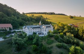 Refugium Hochstrass, © Niederösterreich Werbung / Maximilian Pawlikowsky Luftaufnahme eines großen weißen Gebäudes in einer grünen Landschaft.