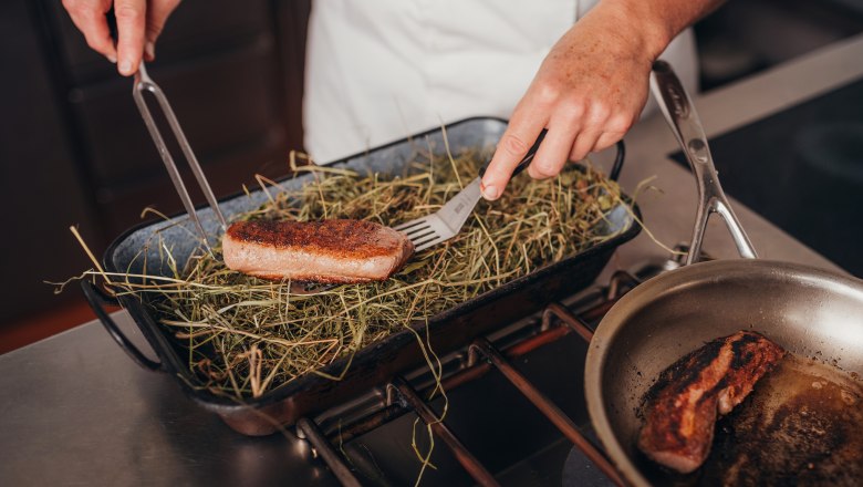 Saddle of venison braised in a bed of hay, © Niederösterreich Werbung/Daniela Führer A cook places a piece of saddle of venison on a bed of hay in a roasting tin.