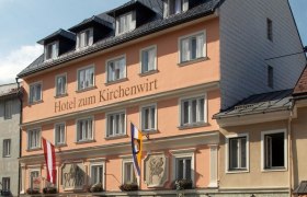 Hotel zum Kirchenwirt, © zVg Hotel zum Kirchenwirt Fassade des Hotels zum Kirchenwirt mit Fahnen und blauer Himmel.