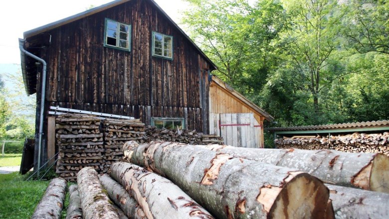 Holzknechtmuseum Trübenbach, © weinfranz.at Holzstapel und Baumstämme vor einem rustikalen Holzgebäude im Freien.