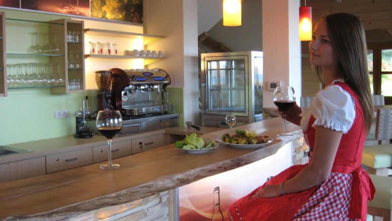 An der Bar in der Höhenstein Stube, © Fam. Helmel Frau in traditioneller Kleidung sitzt an einer Bar mit einem Glas Rotwein.