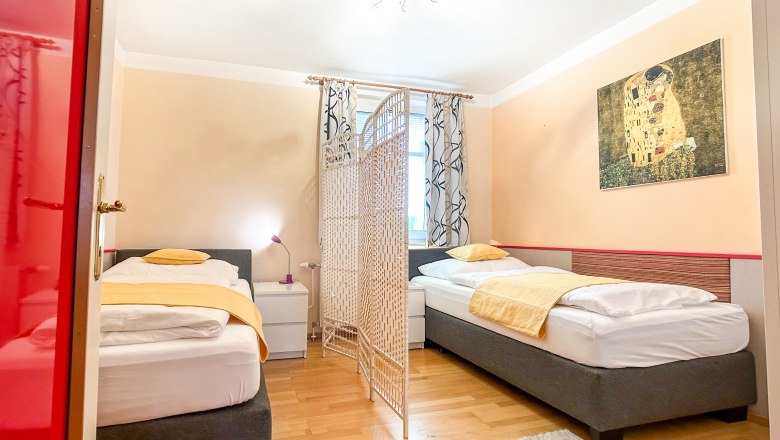 Haus Morgensonne Schlafzimmer, © Fam. Pauker Schlafzimmer mit zwei Einzelbetten, gelber Bettwäsche, einem Raumteiler und einem Gemälde an der Wand.