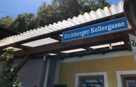 Eichberger Kellergasse, © Donau Niederösterreich Schild mit der Aufschrift 'Eichberger Kellergasse' an einem Gebäude mit Wellblechdach.