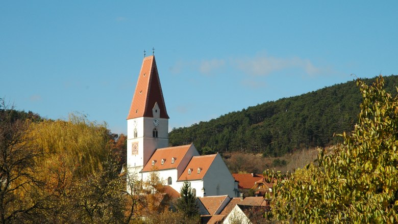 Nußdorf parish church, © Blesl Nußdorf parish church with red roof and clock tower, surrounded by trees and hills.