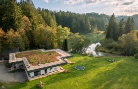 Ferienhaus am See, © Niederösterreich Werbung / Maximilian Pawlikowsky Luftaufnahme eines modernen Hauses mit begrüntem Dach, umgeben von Wald und einem See.