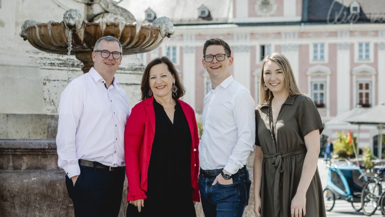 Leo and Brigitte Graf with son Andreas and daughter-in-law Birgit, © Niederösterreich-Werbung/David Schreiber Four people stand smiling in front of a fountain in an urban setting.