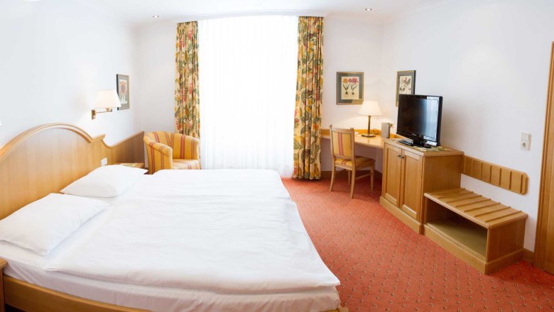 Gasthof zum Schwan, © Gerda Schmidt Ein Hotelzimmer mit Doppelbett, Schreibtisch, Fernseher und Sessel. Helle Vorhänge und florale Vorhänge schmücken das Fenster.