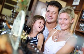Hotel zur Post, © weinfranz.at Eine lächelnde Familie steht in einem Restaurant oder Hotel an der Bar.