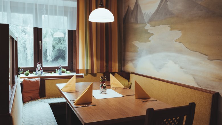 Take a seat and enjoy!, © Niederösterreich Werbung/David Schreiber Cozy seating area with wooden table, yellow napkins and wall painting in a restaurant.