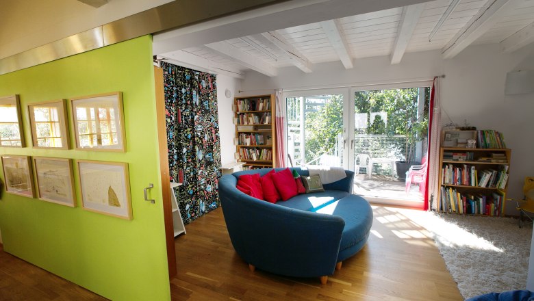 Tailor's cottage, © Doris Schwarz König Interior view of a modern living room with a round blue couch, wooden floor, bookshelves and large windows overlooking a garden.