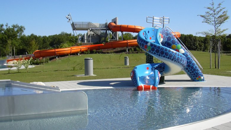 Aquapark, © Stadtgemeinde Herzogenburg Blick auf einen Aquapark mit blauer Kinderrutsche und großer oranger Wasserrutsche im Hintergrund.