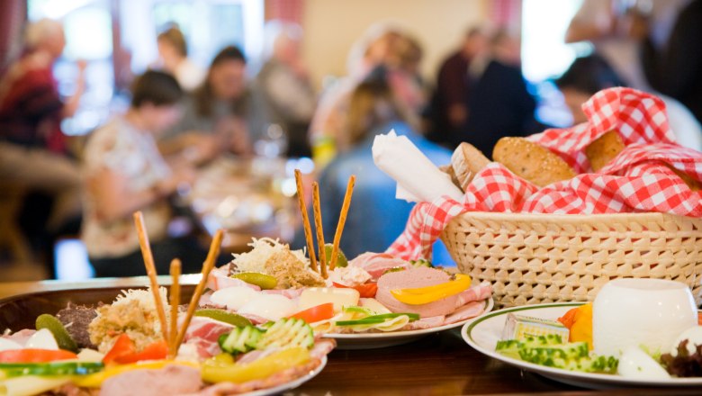 Heurigen snack, © Marius Höfinger A table with traditional Austrian dishes, including cold cuts, cheese and bread in a basket with a red and white checked cloth.