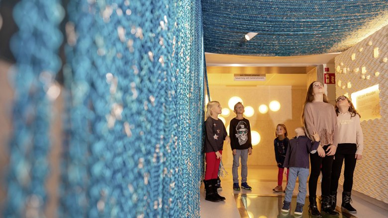 Country of ingredients, © Haubis GmbH Children stand in a room with blue, hanging nets and illuminated walls.