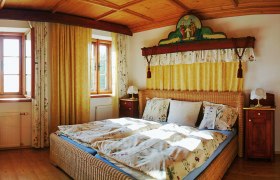 Vierkanter Rabenlehen, © Vierkanter Rabenlehen Gemütliches Schlafzimmer mit Holzmöbeln und Doppelbett, dekoriert mit floralen Mustern und gelben Vorhängen.