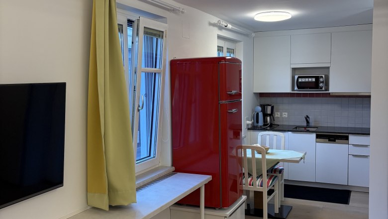 TDR-Haus Morgensonne- Wohnzimmer, © Fam Pauker Modernes Wohnzimmer mit offener Küche, rotem Kühlschrank, gelben Vorhängen und Holzboden.