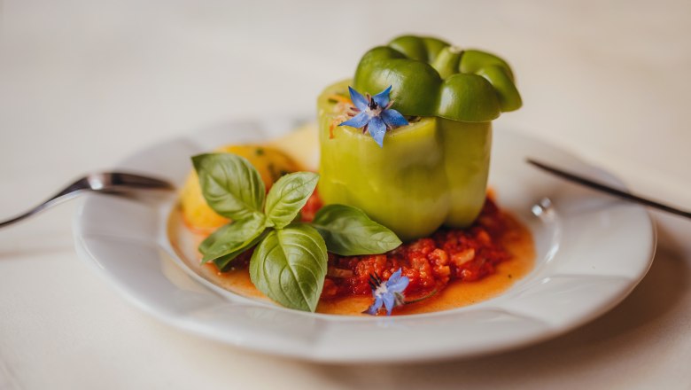 Gefüllter Paprika, © Niederösterreich Werbung/Daniela Führer Gefüllter grüner Paprika auf Tomatensauce, garniert mit Basilikum und blauer Blüte auf einem weißen Teller.
