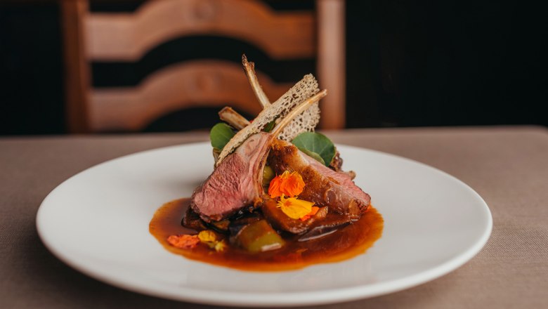 Mostviertel pasture-fed lamb, stuffed mini peppers, watercress and lemon-thyme jus, © Niederösterreich Werbung/Daniela Führer Gourmet dish with lamb, mini peppers, watercress and jus on a white plate.