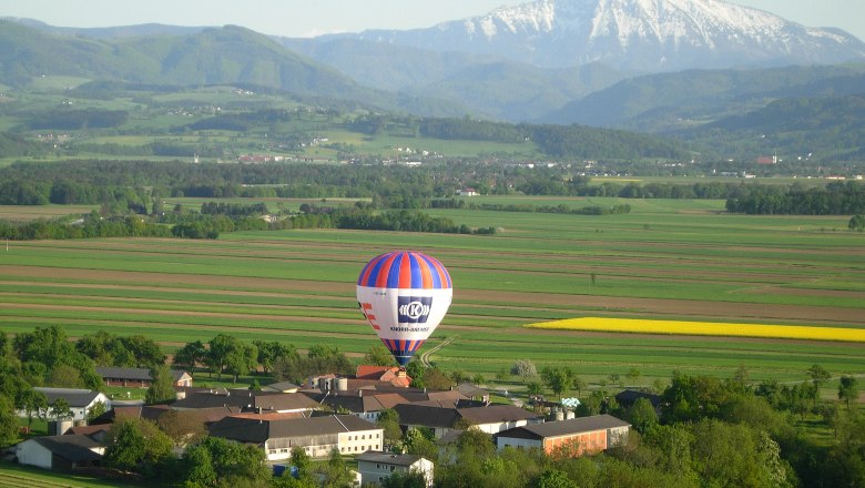 Mit dem Ballon übers Mostviertel fliegen, © Mostviertel Ballooning, Andreas Simoner Heißluftballon über einer ländlichen Landschaft mit Bergen im Hintergrund.
