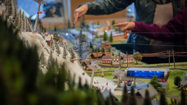 The fascination of model making, © Rene Jagersberger Detailed model landscape with cable car and snow-covered trees, two people pointing at the model in the background.