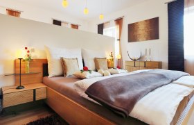 Straußenhof Ebner, © weinfranz.at Gemütliches Schlafzimmer mit Doppelbett, dekoriert mit Kissen und Rosen, Holzmöbeln und sanfter Beleuchtung.